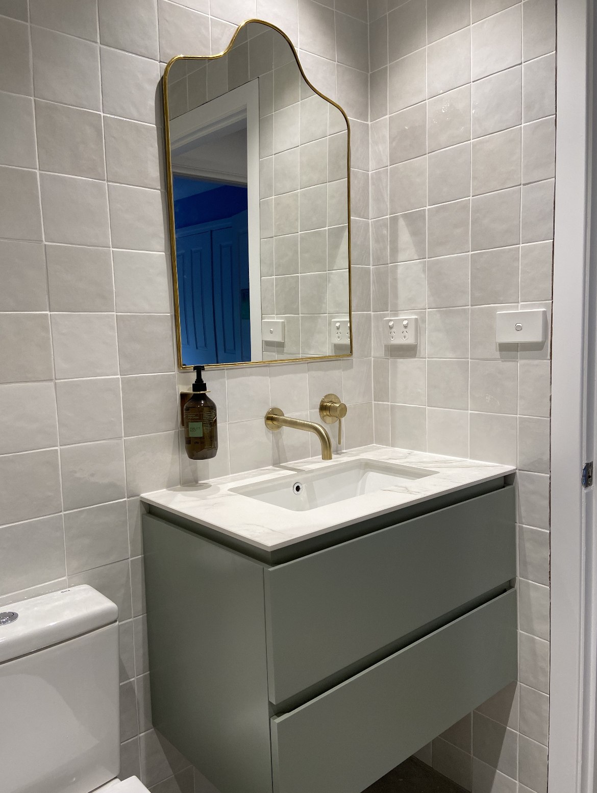 Sage-green vanity with brushed gold tapware and mirror